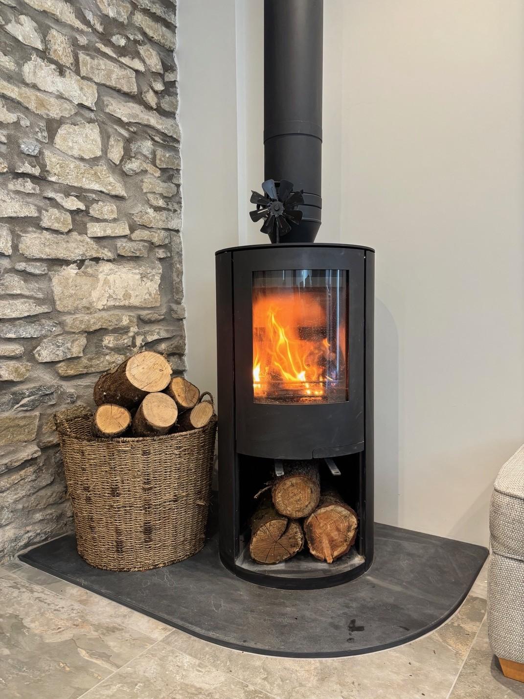 The wood burner, lit, with a basket of logs beside it